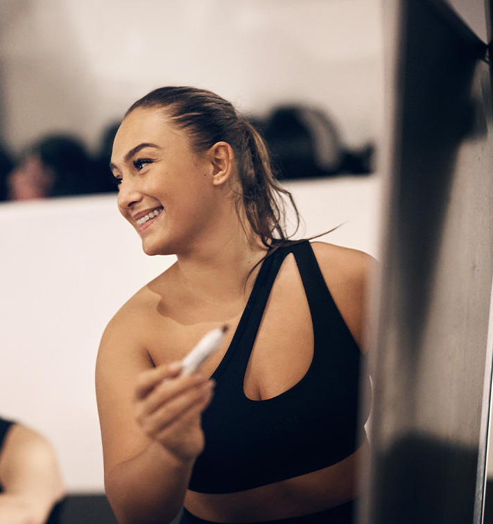 Coachen smiler i et fitnesscenter med en telefon i hånden
