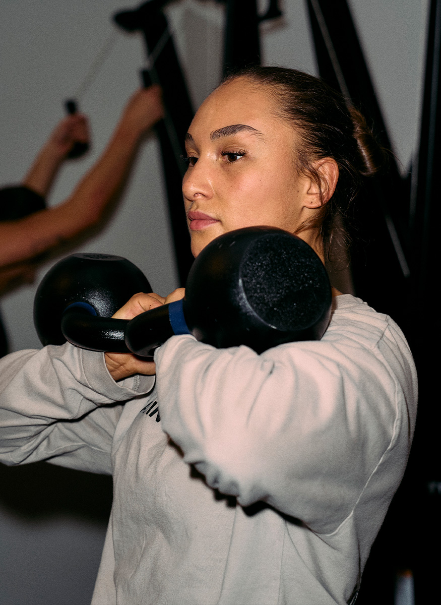 Coachen løfter to kettlebells i brysthøjde i et fitnesscenter